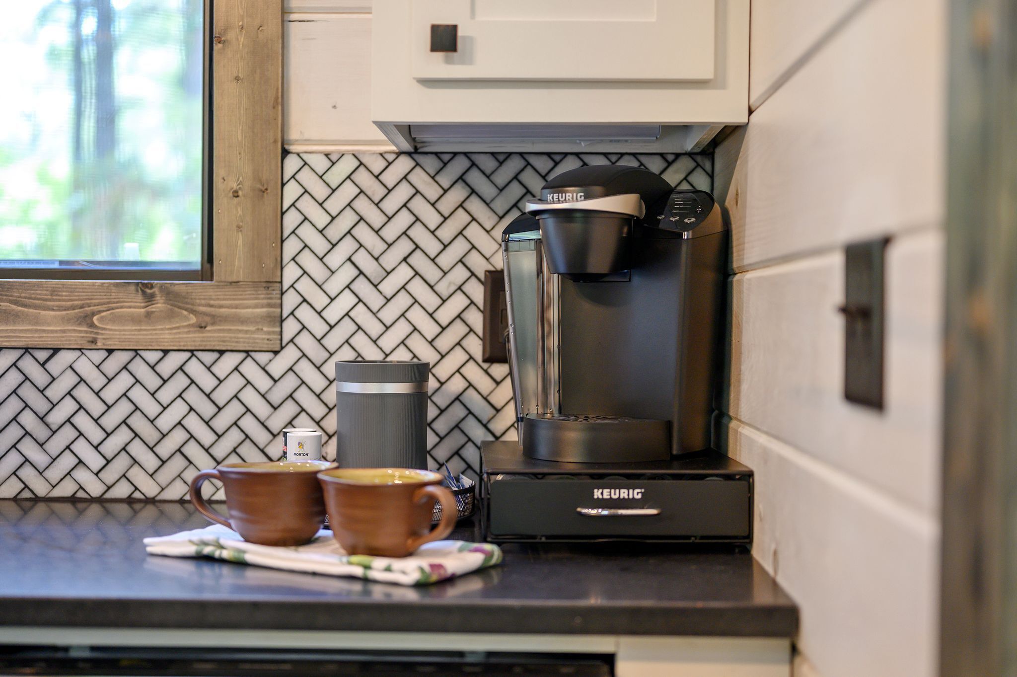 A kitchen with a coffee maker, two cups, and a kettle on the counter.