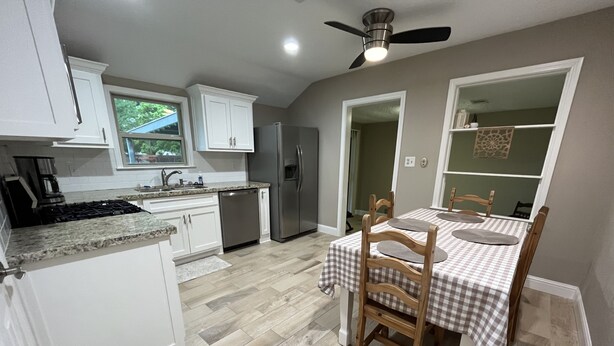 A kitchen with white cabinets, a stainless steel refrigerator, and a dining area with a checkered tablecloth. - The Nest - 2 beds, 1 bath - Quiet & Comfortable  (Groves)