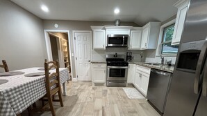 A kitchen with white cabinets, stainless steel appliances, a checkered tablecloth, and a wooden dining table. - The Nest - 2 beds, 1 bath - Quiet & Comfortable  (Groves)