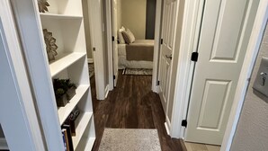 A narrow hallway with a patterned rug, white shelving units, and a bed in the background. - The Nest - 2 beds, 1 bath - Quiet & Comfortable  (Groves)