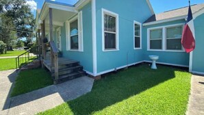 A two-story house with a porch, a small front yard, and a flag on the right side. - The Nest - 2 beds, 1 bath - Quiet & Comfortable  (Groves)