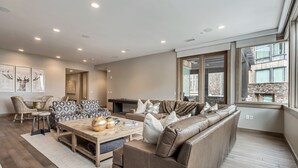 A modern living room with a brown leather sofa, a wooden coffee table, and a dining area with wicker chairs. - Premium Five Bedroom Suite 5 Apartment Hotel by Redawning (Park City)