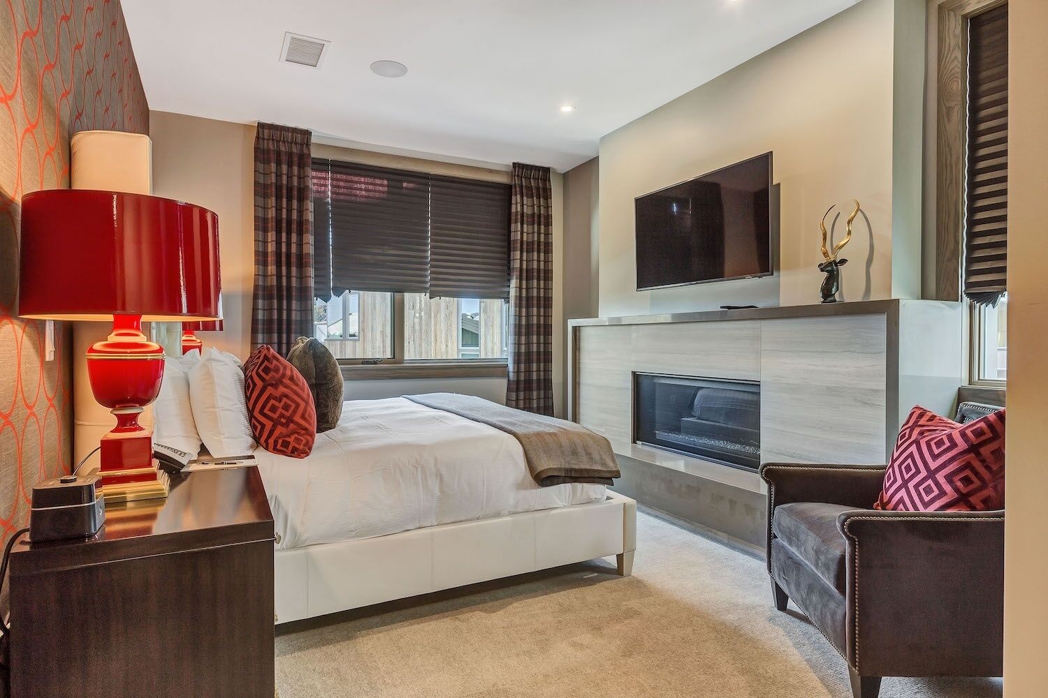 A modern hotel room with a bed, a TV, a fireplace, and a seating area.