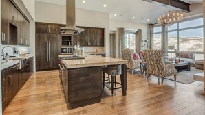 A modern kitchen with dark wood cabinets, a large island, and a dining area with patterned chairs. - Four Bedroom Penthouse 4 Apartment Hotel by RedAwning (Park City)