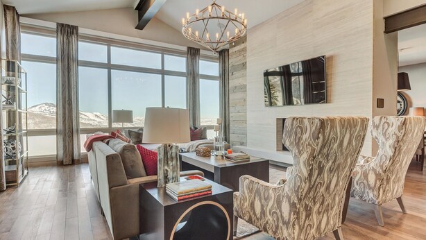 A modern living room with a large window, a chandelier, and a sofa with a side table. - Four Bedroom Penthouse 4 Apartment Hotel by RedAwning (Park City)