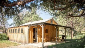 Een houten chalet met een overdekte veranda, een eethoek en een barbecue.