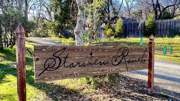 Een houten bord met de naam 'Starville Ranch' in sierletters, bevestigd aan twee houten palen.