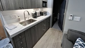 Een compacte keuken met donkerhouten kastjes, een wit aanrecht, een ingebouwde magnetron en een spoelbak.