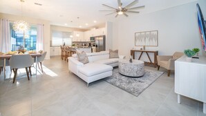 Una sala de estar moderna con un sofá blanco, una mesa de comedor y una cocina al fondo.