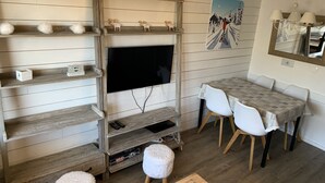 A cozy living room with a TV, wooden shelves, a dining table with chairs, and a ski-themed wall decoration. - Rental Apartment 2 room 26 M2 - Alps - Avoriaz - Douchka - Falaise (Morzine)