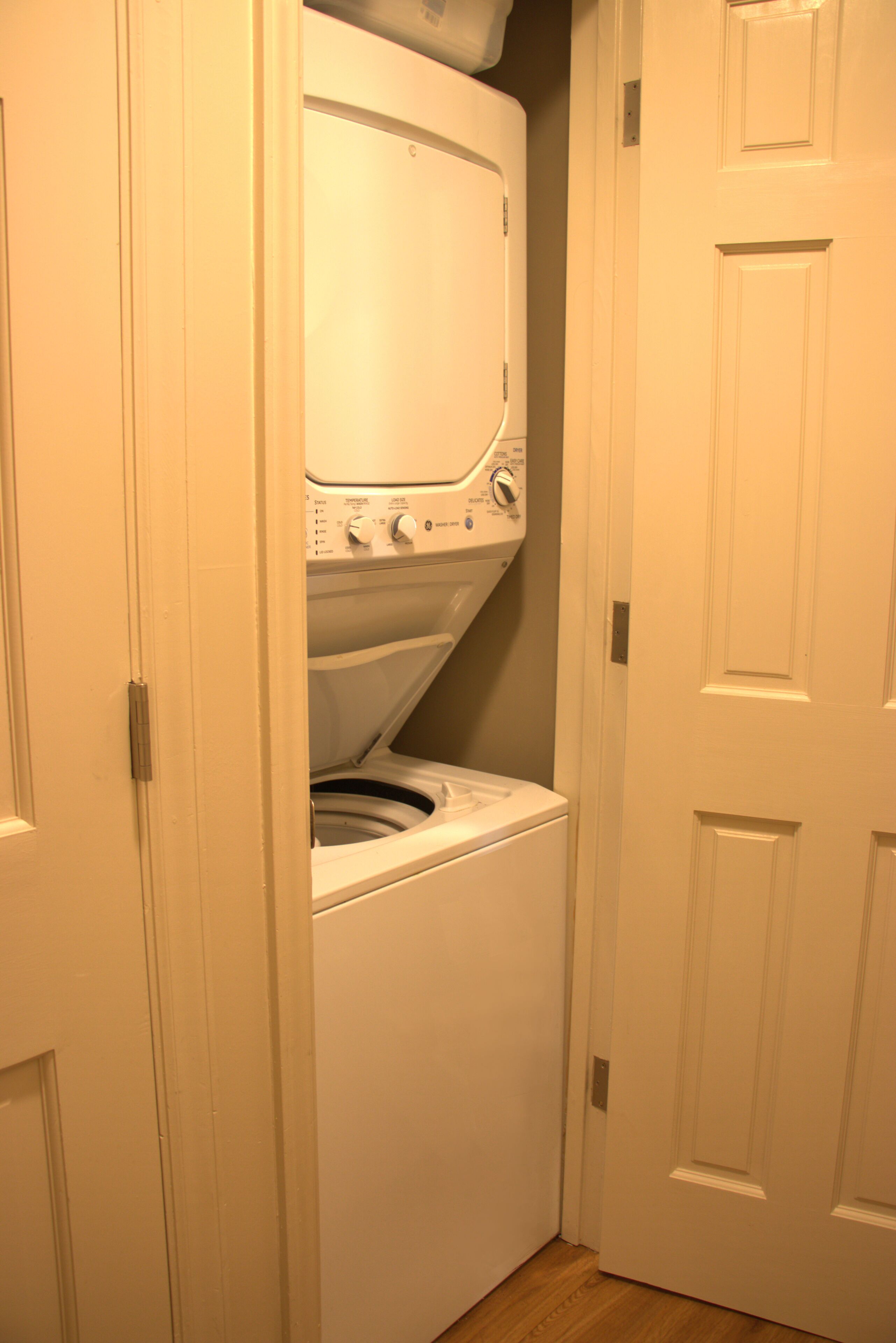 A laundry room with a front-loading washer and dryer, a door, and a wooden floor.