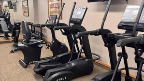 Ein Fitnessstudio mit mehreren Laufbändern, Kraftgeräten und einem an der Wand befestigten Fernseher.