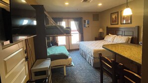 Ein Hotelzimmer mit einem Bett, einem Schreibtisch mit Stuhl, einem Fernseher, einem Fenster mit Vorhängen und einem Deckenventilator.
