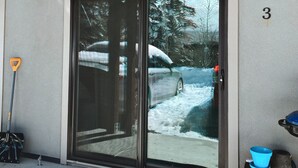 Un numéro de maison, le chiffre « 3 », sur un mur à texture, une porte coulissante en verre, une pelle en métal, un seau bleu et un tonneau en bois.