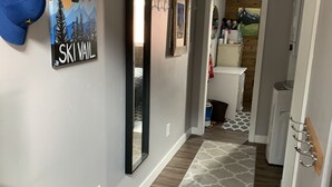 Un couloir avec un tapis à motifs, une œuvre d’art sur le thème du ski et un miroir.