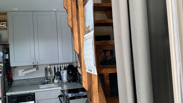 Une cuisine avec des meubles blancs, un lave-vaisselle en acier inoxydable et un escalier en bois.