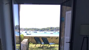 A room with a desk, a laptop, and a view of a harbor with boats. - Location Saisonnière Île Tudy « Sur Leau » (Île-Tudy)