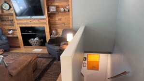 Ein Wohnzimmer mit Sofa, Fernseher, Kamin und einer Treppe zu einer Ebene darunter.