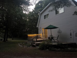 A house with a deck, outdoor lighting, and a table with an umbrella. - M-22 home, 3 min to Lake Michigan and surrounded by hiking trails! (Frankfort)