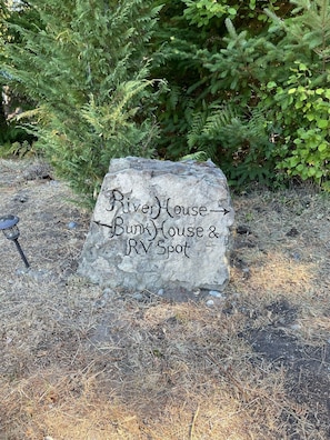 Une pancarte en pierre indiquant les directions vers River House, Bunk House et l’aire de stationnement pour les véhicules de loisirs.