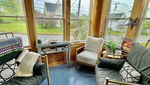 A cozy room with a wooden ceiling, large windows, a blue tiled floor, a sofa, a chair, and a small table with a plant.