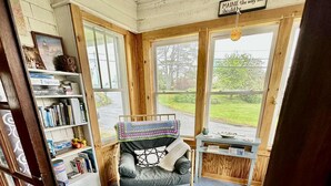 A cozy room with a bed, a bookshelf, and large windows offering a view of the outdoors.
