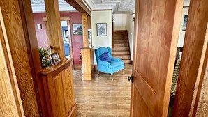 A wooden hallway leading to a staircase, with a blue chair and a framed picture on the wall.