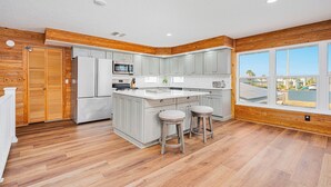 A kitchen with a large island, wooden paneling, and a view through large windows.