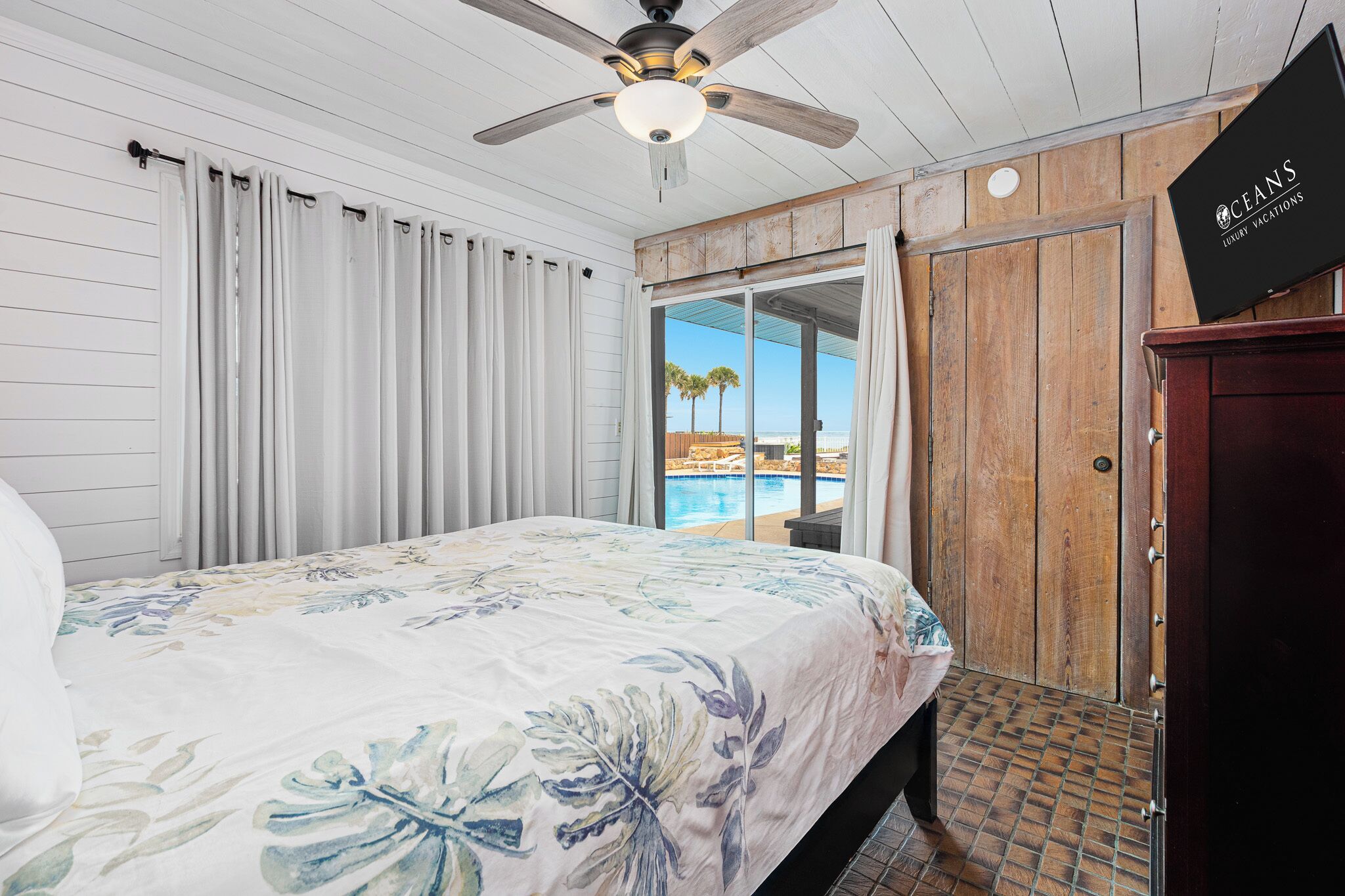 A bedroom with a bed, a ceiling fan, a view of the pool, and a wooden door.