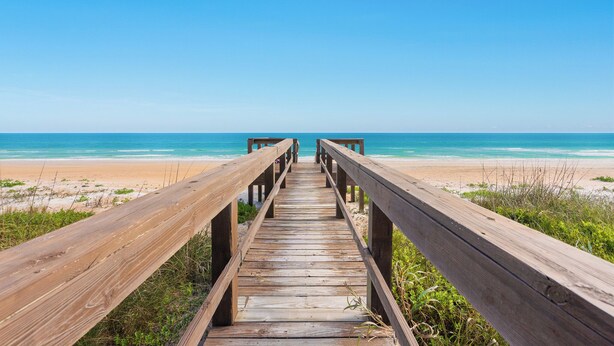 A wooden boardwalk leading to a beach with clear skies.