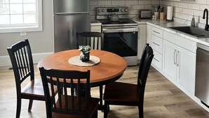 A modern kitchen with white cabinets, stainless steel appliances, and a wooden dining table with chairs. - The Barron Historic Eau Claire Home (Eau Claire)