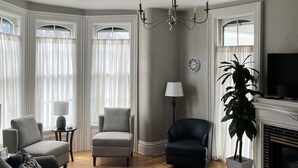 A living room with a fireplace, a chandelier, and a television. - The Barron Historic Eau Claire Home (Eau Claire)
