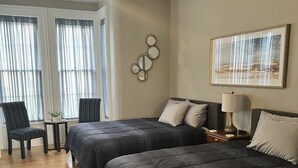 A hotel room with two beds, a ceiling fan, a framed picture on the wall, and a chair by the window. - The Barron Historic Eau Claire Home (Eau Claire)
