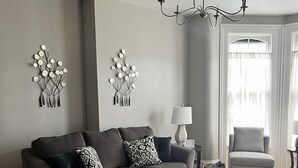 A living room with a grey sofa, a round coffee table, a chandelier, and wall art. - The Barron Historic Eau Claire Home (Eau Claire)