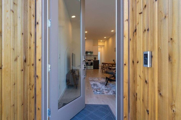Un intérieur moderne avec un mur en bois, une porte en verre donnant sur un coin repas et une cuisine en arrière-plan.