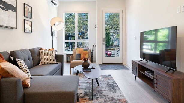 A modern living room with a grey sofa, a coffee table, a TV, and a large window. - Perch - Urban Reflections 13: WS 97! Spacious 3BR/2BA w Space Needle view (Seattle)