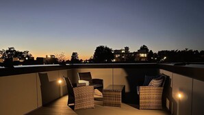 A rooftop terrace with wicker furniture and a view of the city skyline at dusk. - Perch - Urban Reflections 13: WS 97! Spacious 3BR/2BA w Space Needle view (Seattle)
