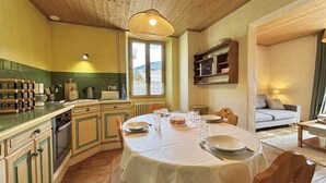 A cozy kitchen with wooden cabinets, a dining table set for four, and a view of the outdoors through a window. - Ground floor, tv, ski locker, 42m², Praz sur Arly (Praz-sur-Arly)