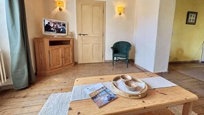 A cozy room with a wooden floor, a wooden table with a magazine and bowls, a television on a wooden cabinet, and a green chair. - Ground floor, tv, ski locker, 42m², Praz sur Arly (Praz-sur-Arly)