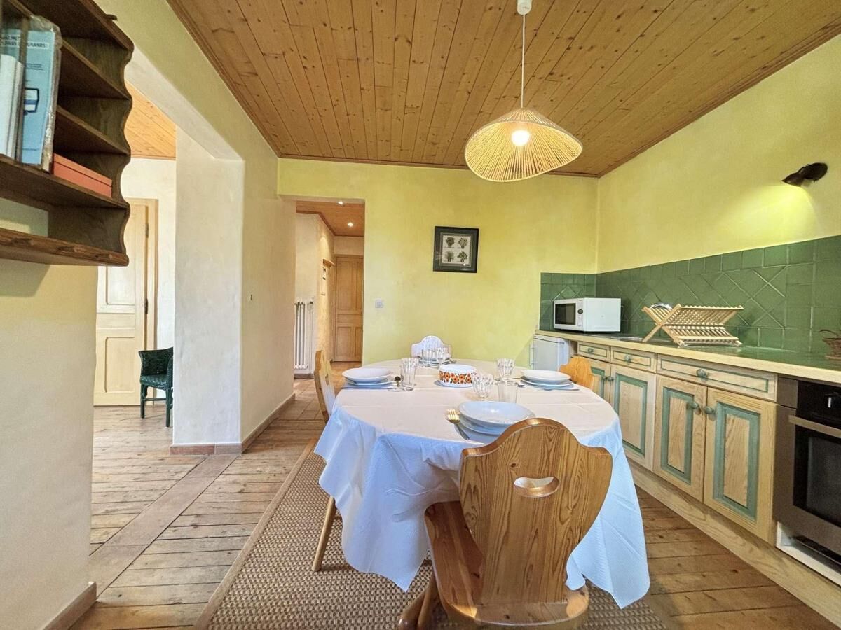 Un coin repas avec une table dressée pour quatre personnes, un plafond en bois et une cuisine aux carreaux verts et dotée d’un four à micro-ondes.
