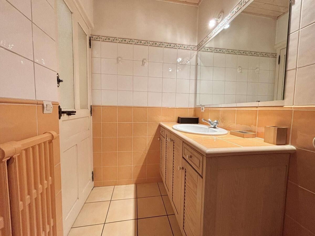Un baño con una puerta blanca, azulejos color beige, un radiador de madera, un lavabo y un espejo.