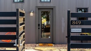Un edificio moderno con fachada gris, una puerta de acceso numerada y un felpudo con la inscripción 'HEY YALL'.
