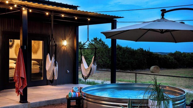 Un área de piscina moderna al aire libre con un jacuzzi, sillones colgantes e iluminada con luces tipo guirnalda.