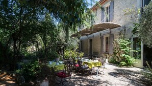 Un patio al aire libre con mesas y sillas, rodeado de follaje y un edificio de piedra.