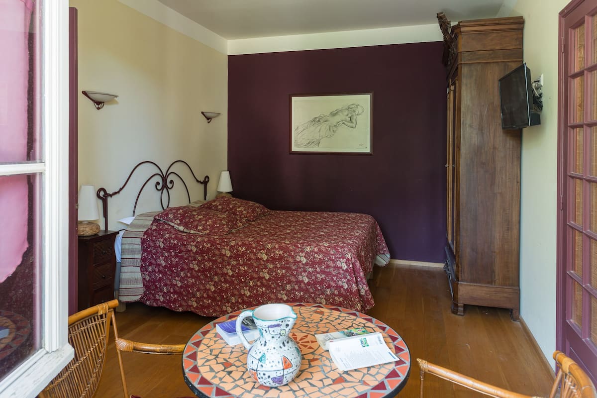 A bedroom with a bed, a wooden wardrobe, a table with a jug, and a framed picture on the wall.