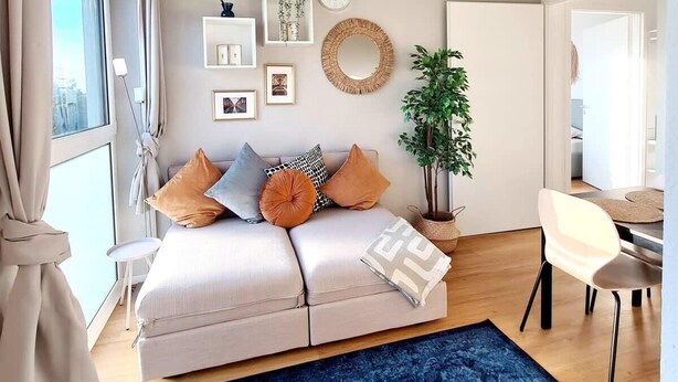 A modern bedroom with a bed, bedside tables, a dresser, a large window, and a view of the city.