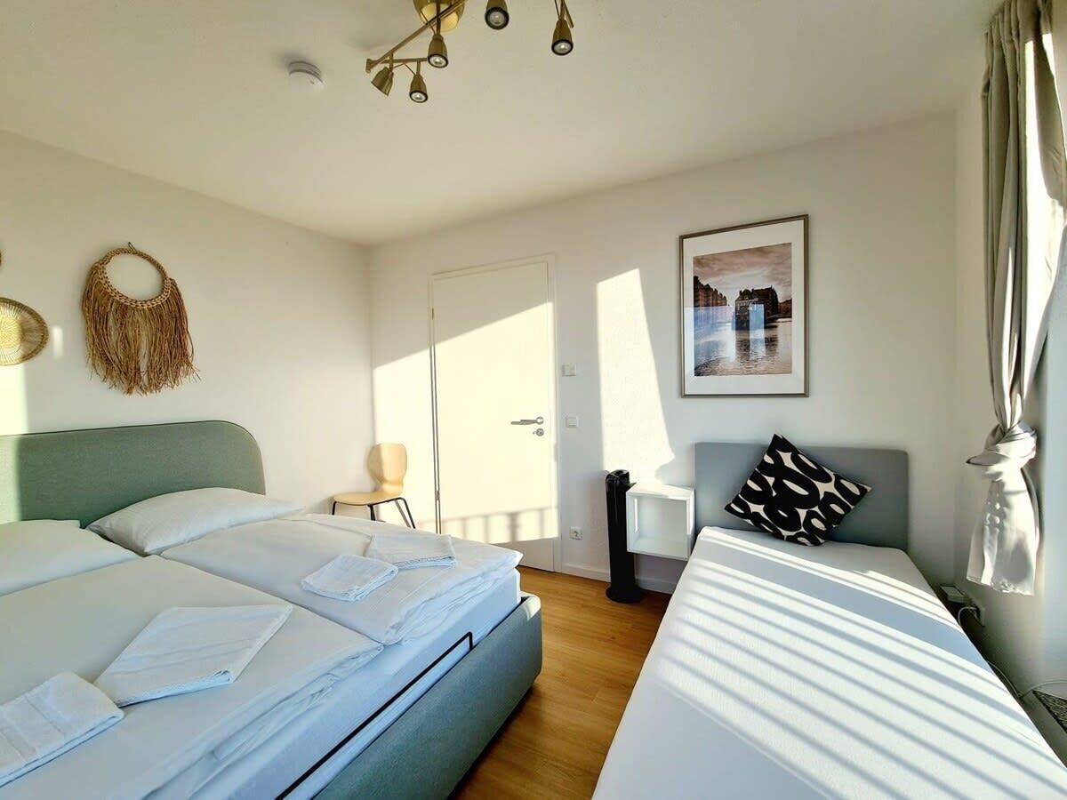 Camera d'albergo con due letti, un tavolino, una sedia, un quadro appeso alla parete e una porta che dà su un balcone.