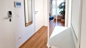 A hallway with a white door, a digital lock, a mirror, and a white shelf unit.