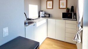 A compact kitchen with a sink, microwave, and a small countertop. There are two framed pictures on the wall and a ceiling light fixture.