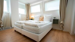 Un lit bien fait, avec des draps blancs et deux oreillers, un plancher en bois et une fenêtre avec des rideaux.